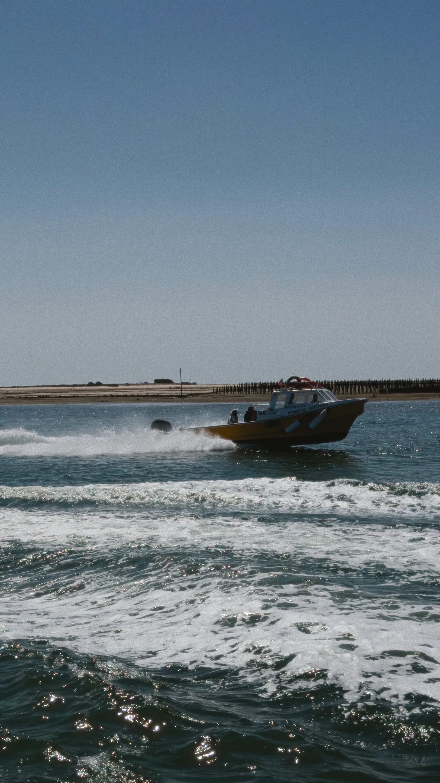 A yellow water taxi speeding across the channel, leaving a broad trail of white spray behind it.