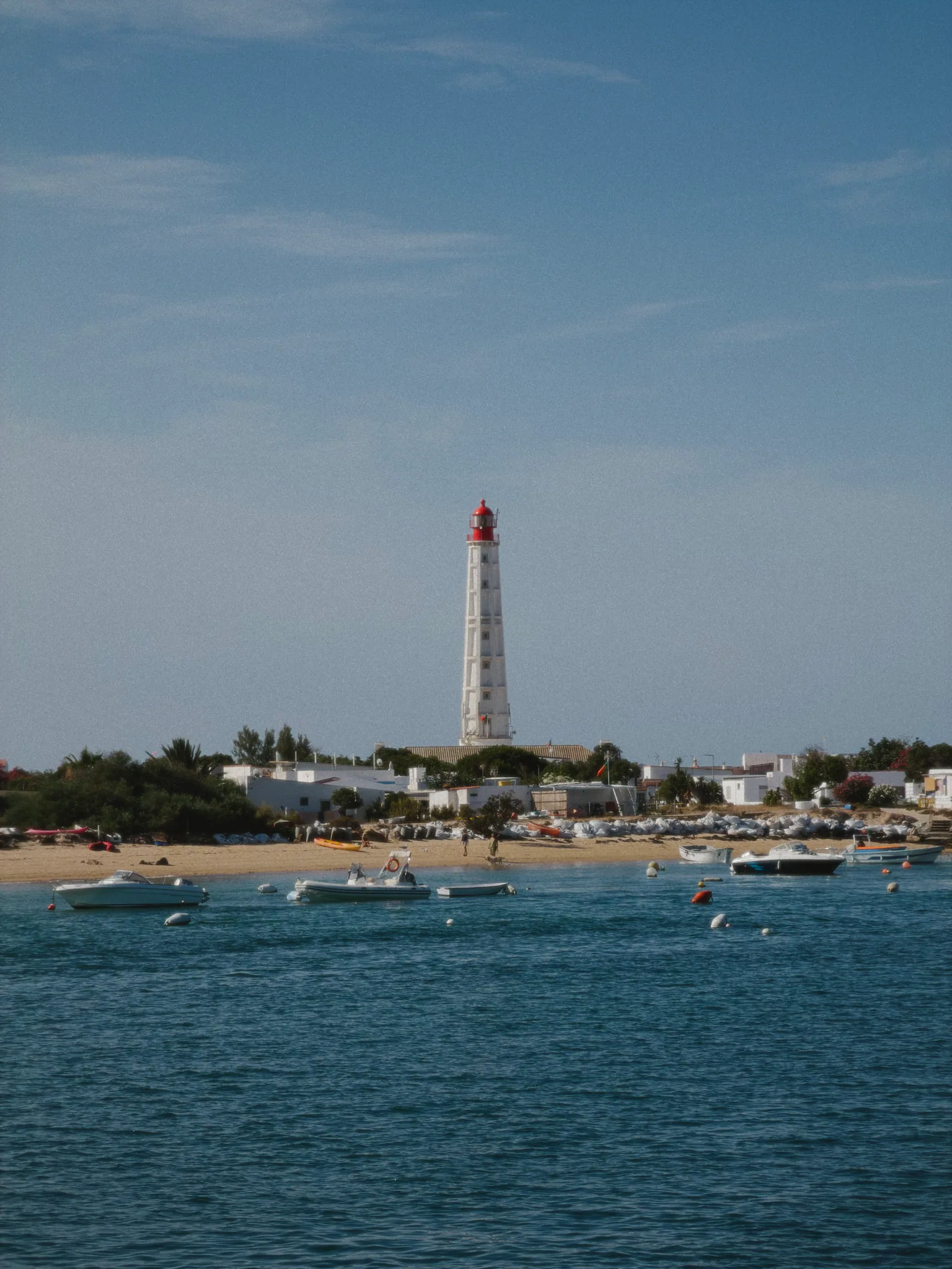 The Farol lighthouse rising above white houses and anchored boats across the water.