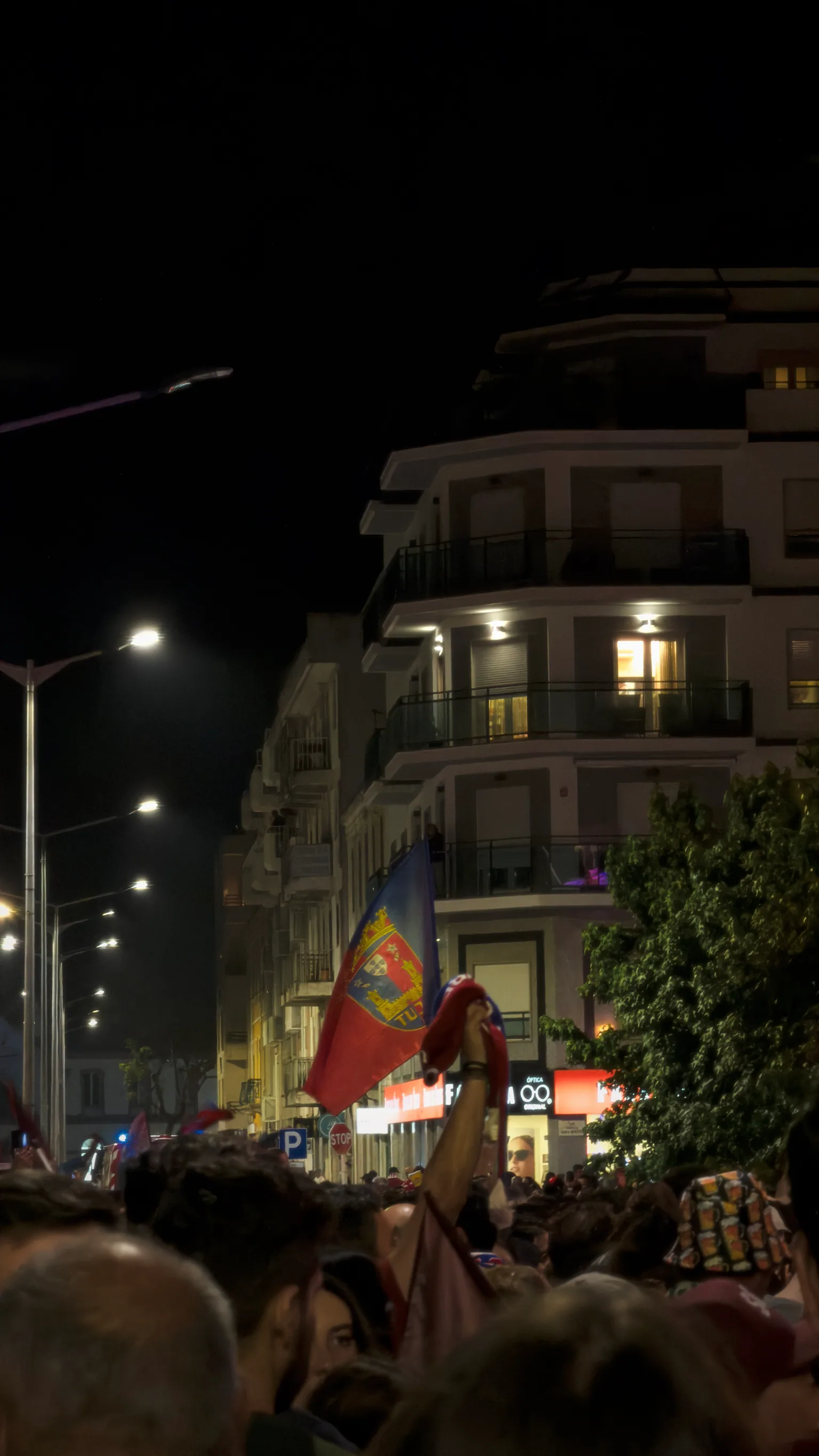 A Torreense flag rising above a tightly packed crowd celebrating at night in Torres Vedras