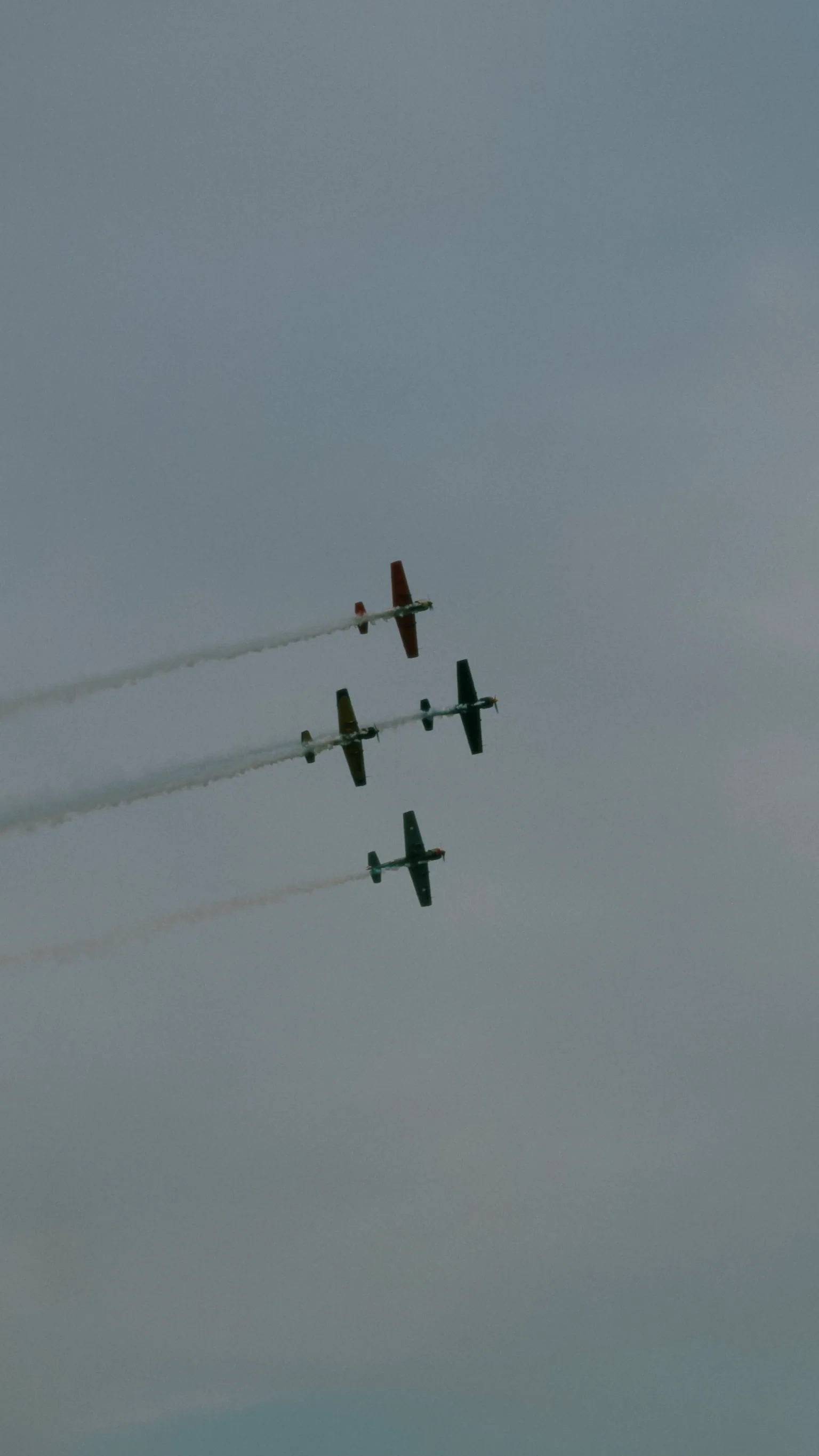 Four aircraft flying in formation and leaving smoke trails across an overcast sky