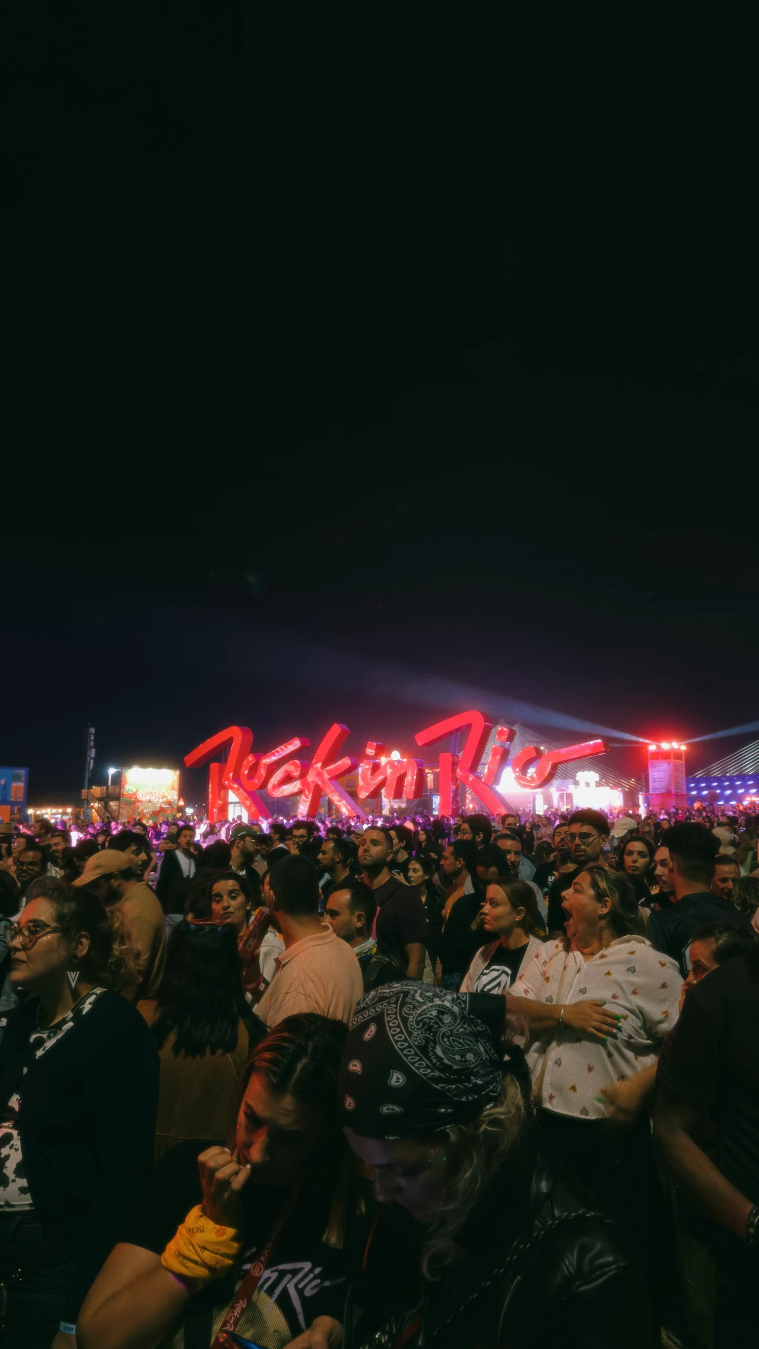 A dense nighttime crowd gathered beneath the illuminated Rock in Rio sign