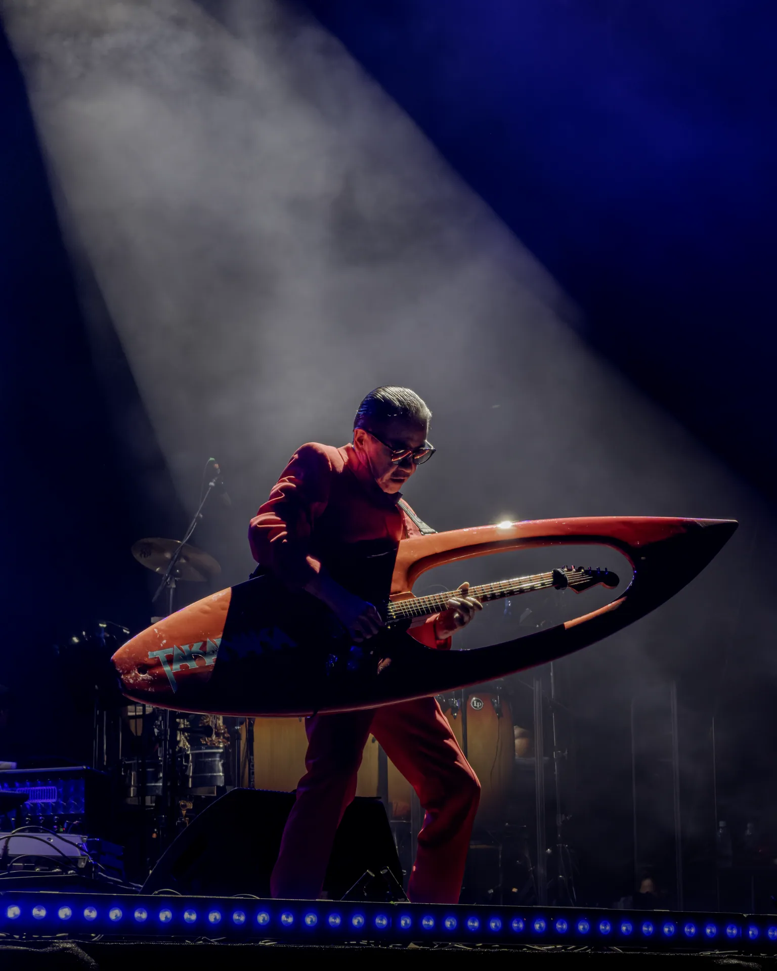 Masayoshi Takanaka performing under a spotlight with a guitar built into a giant red surfboard.
