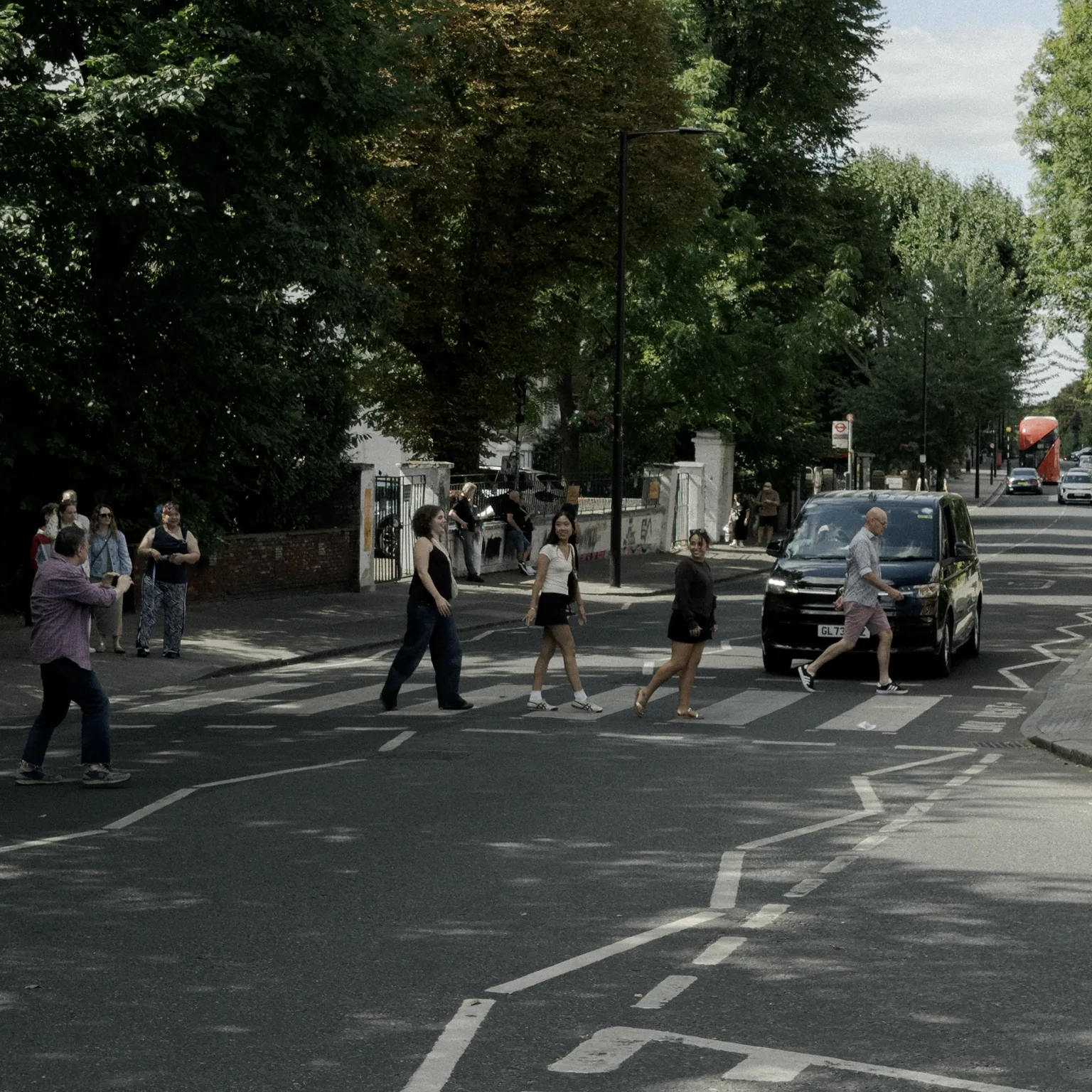Four strangers crossing Abbey Road together while a person on the pavement raises a camera to photograph them.